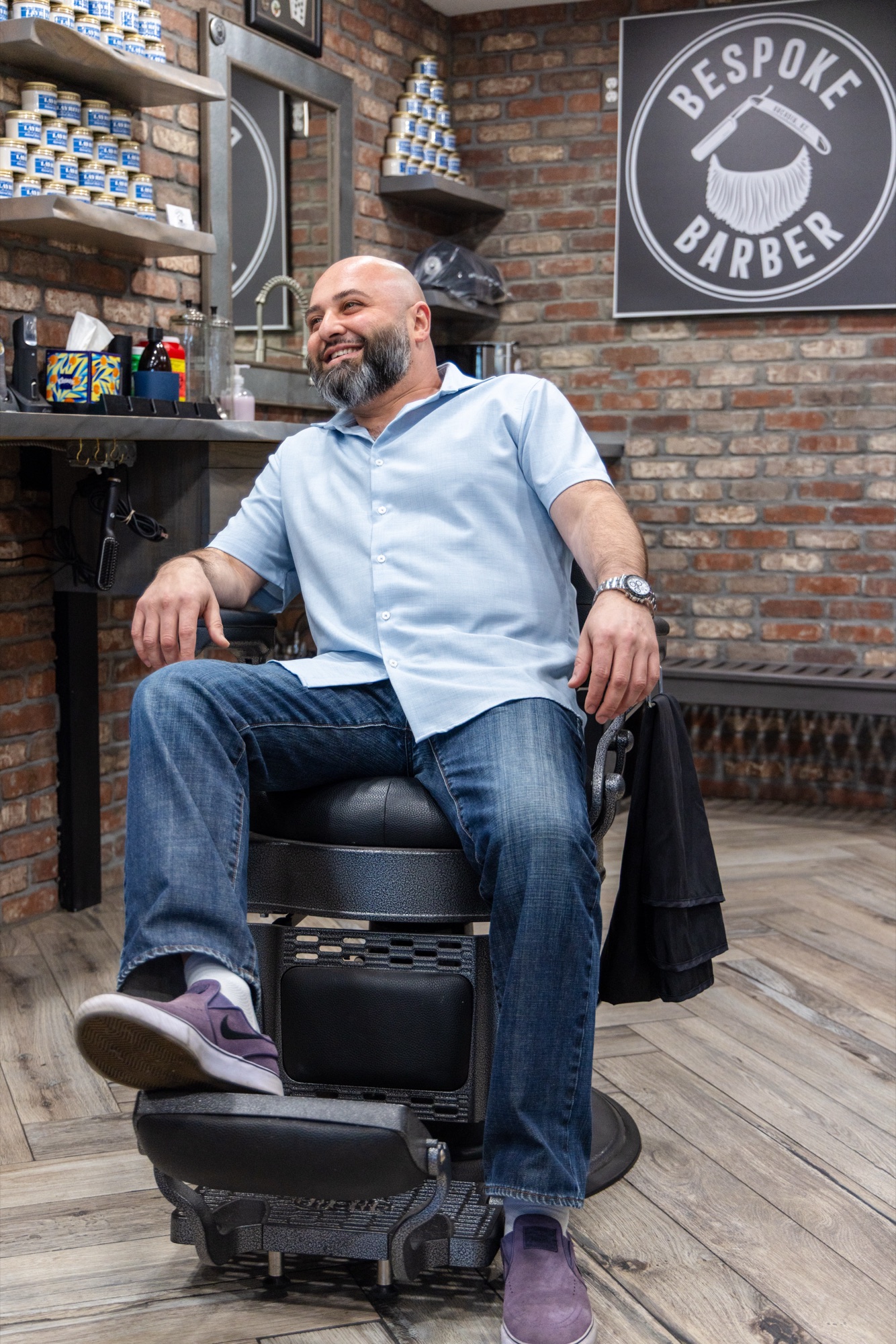 Boris sitting in the classic barber chair in front of the Bespoke Barber sign