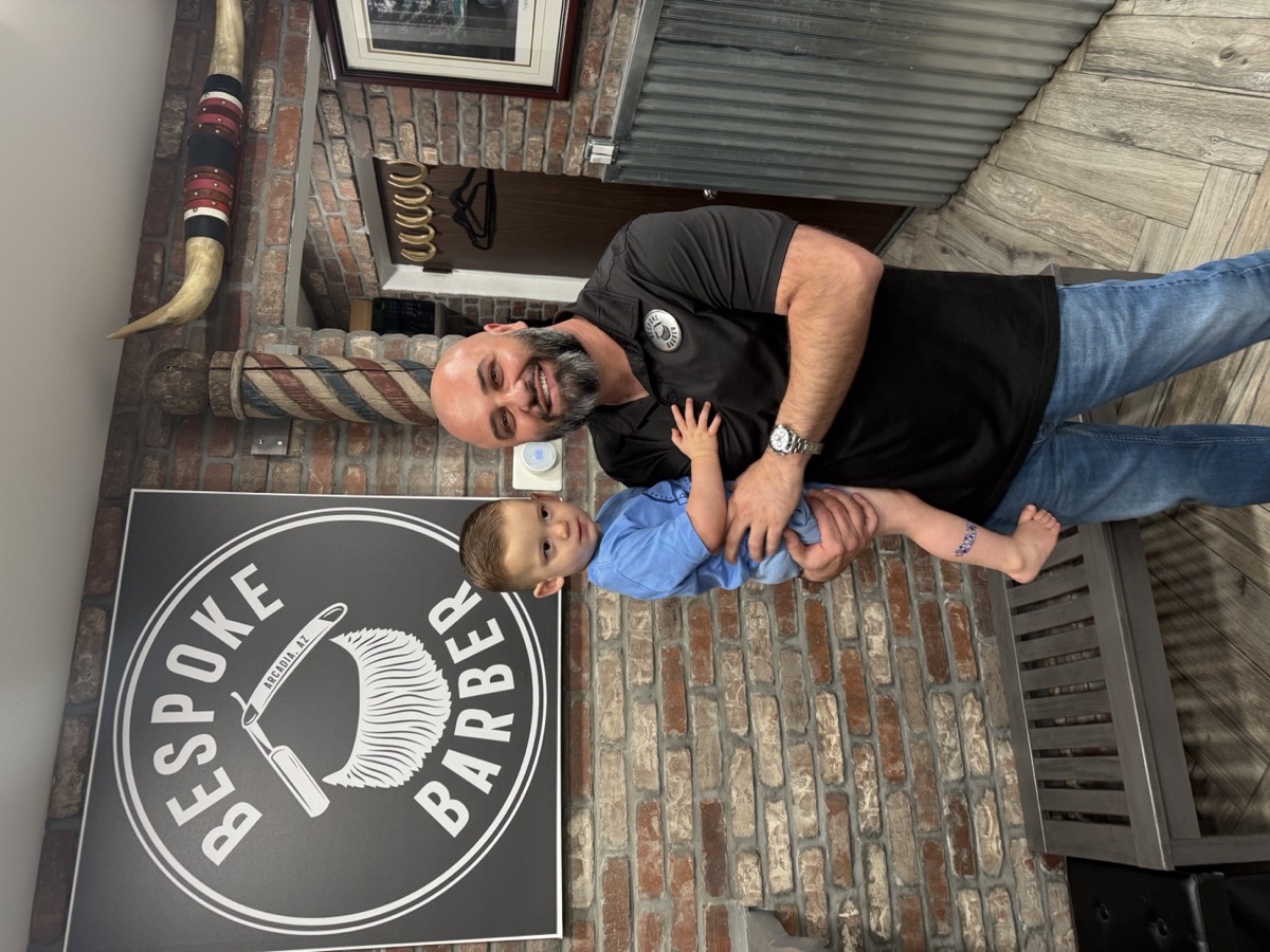 Boris holding a toddler in front of the Bespoke Barber sign