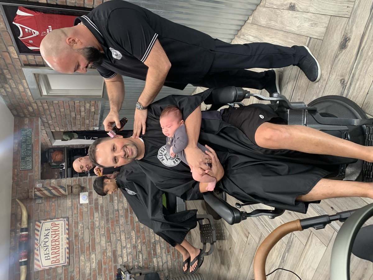 Boris cutting hair while client holds his newborn baby — trust runs deep