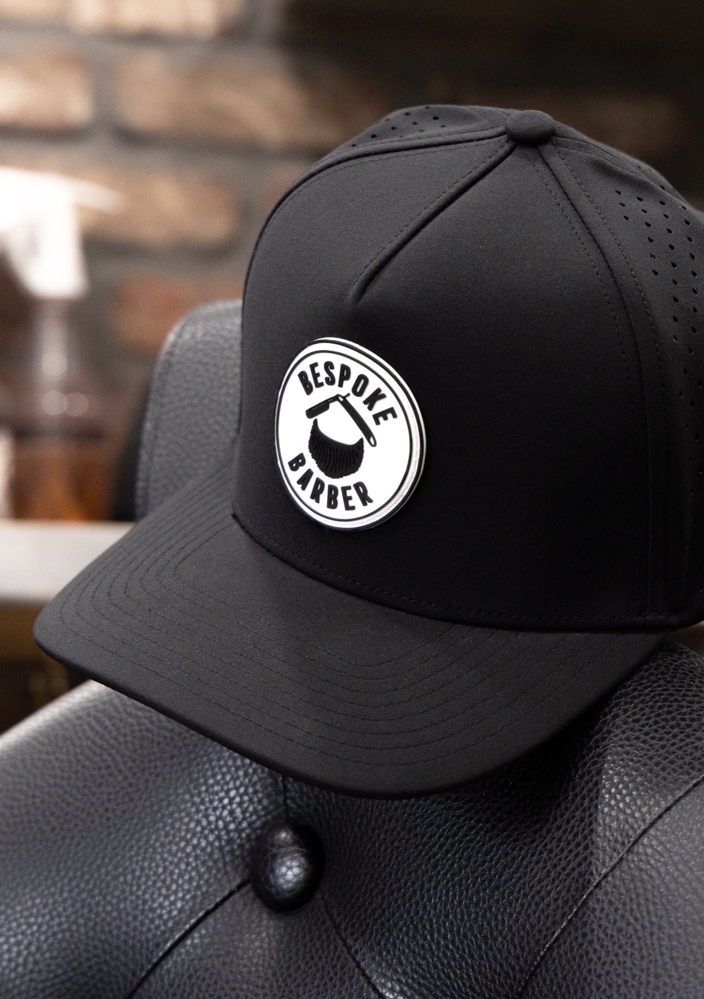 Bespoke Barber branded snapback hat resting on the classic leather barber chair