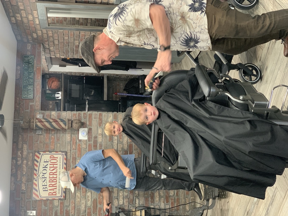 Boris cutting a child's hair while another kid waits — family atmosphere